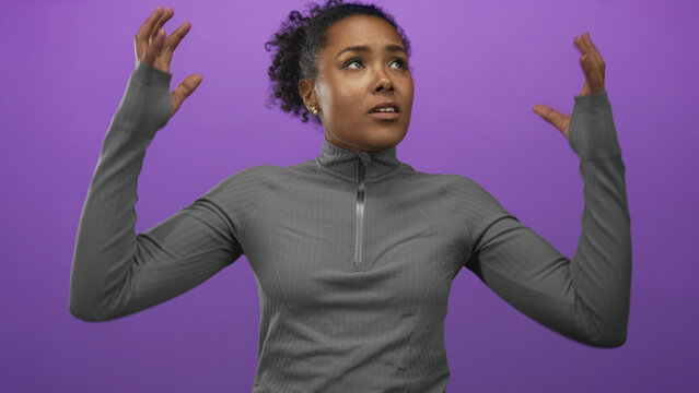 Young woman frowning with arms akimbo wearing gray pullover in purple studio; frustration stress tension.