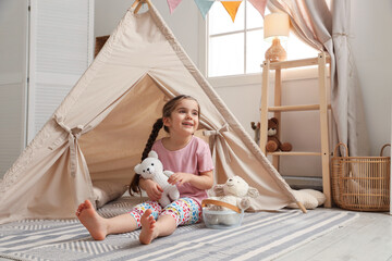 Little girl playing with toys near toy wigwam in playroom, space for text © New Africa