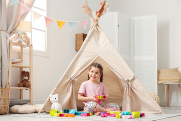 Little girl playing with building blocks near toy wigwam in playroom © New Africa