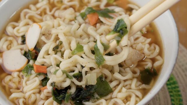 Instant ramen bowl with vegetables fish cake and chopsticks in broth close up asian noodle soup ready to eat quick meal concept japanese style food. 