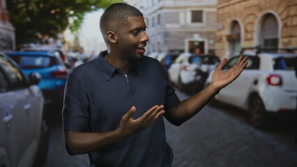 Obraz premium Man showing open hands and speaking while looking aside on a busy city street with parked cars and stone buildings; curiosity conversation.