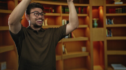 Man cupping hand to mouth calling out toward bookshelves in a warm library interior while smiling and gesturing upward  excitement learning. © Krakenimages.com