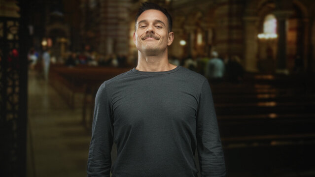 Man with moustache smiling and touching his head amid wooden church pews inside a building; contentment reflection.