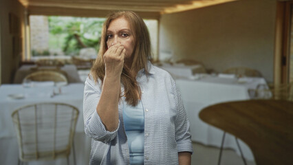 Fototapeta premium Woman pinching fingers to mouth and touching hair in a restaurant dining area inside a building; skepticism contemplation.