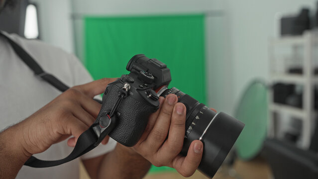 Man holding mirrorless camera with lens and pointing finger to dial against green backdrop in studio; concentration skill craft.