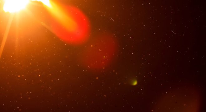 Orange light beam shining through particles in dark space with red glow and lens flare effect