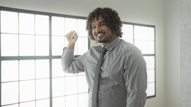Man holds house key and raises fist in celebration inside building, smiling with curly hair; new home joy.