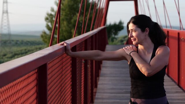 Woman Stretching and Warming Up Before Running on Red Bridge