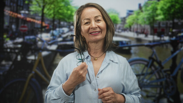 Woman holding eyeglasses near chest on street with bicycles and canal; contentment travel nostalgia.