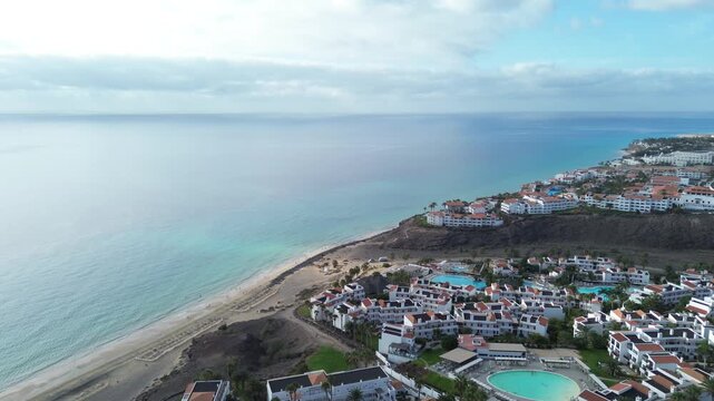 Aerial drone view of a large beachfront resort complex with swimming pools and terraced white buildings on the coast of Costa Calma, Fuerteventura, Canary Islands, Spain