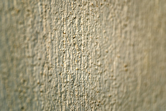 Extreme close up of a highly textured exterior concrete wall coated in light yellowish paint demonstrating a rough bumpy finish perfectly suited for architectural backgrounds