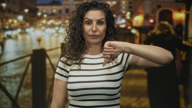 Woman on a bustling city street holds out a hand with thumbs down gesture as traffic flows behind her; disappointment.