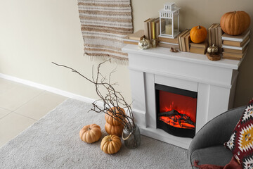 Naklejka premium Interior of light living room with white fireplace, soft armchair, pumpkins and books