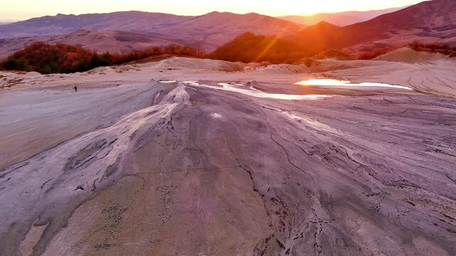 Aerial view of Vulcanii Noroiosi Paclele Mici mud volcanoes with cracked earth and flowing mud under a golden sunset in Scortoasa, Buzau County, Romania.