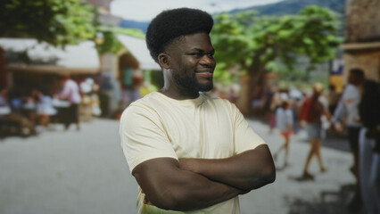 Fototapeta premium Man standing with crossed arms and visible forearms in a busy outdoor street market, smiling at camera; confidence community.
