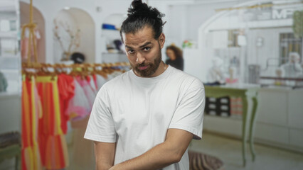 Obraz premium Man smiling and pointing to shoulder while wearing a white t shirt inside a clothing store building with colorful racks and a boutique counter; playful shopping.