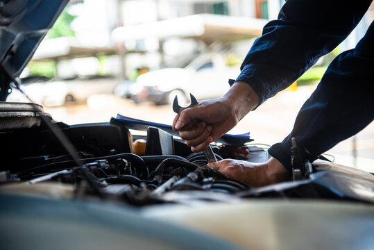 Close up Mechanic man hands repairing car auto repair shop uses jack change tyre. Open vehicle hood checking up auto mobile. Man hands fixing Shock absorber machinery vehicle mechanical service