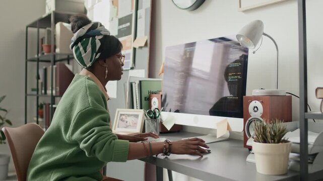 African American woman in vibrant casual clothes intently writing code on computer in bright modern office