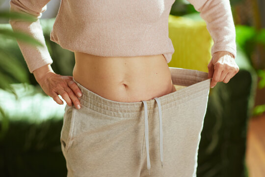 Close-up of a woman pulling her loose waistband to show weight loss results after a successful diet and exercise routine.