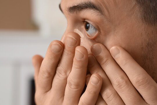 Young man putting in contact lenses at home, closeup