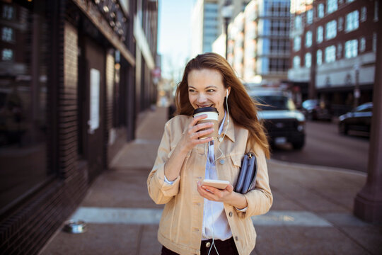 Smiling woman drinking coffee while walking on city street