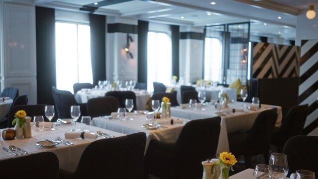 Dining room blurred bokeh interior showing arranged tables, glassware and floral accents with shallow depth of field and soft ambient lighting; background copyspace backplate calm.