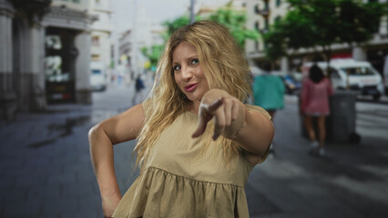 Fototapeta premium Woman points finger at camera on a city street with hand on hip and visible bare hand; playful confidence.