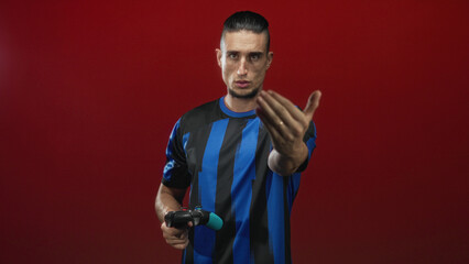 Man holding gamepad points hand toward camera and beckons while wearing soccer jersey in studio  competitive focus. © Krakenimages.com