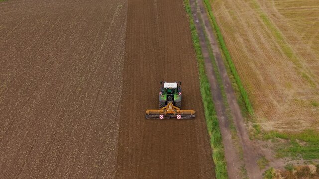 Tractor Tilling Field: An aerial view captures a tractor cultivating a large agricultural field, preparing the soil for planting under a clear sky.