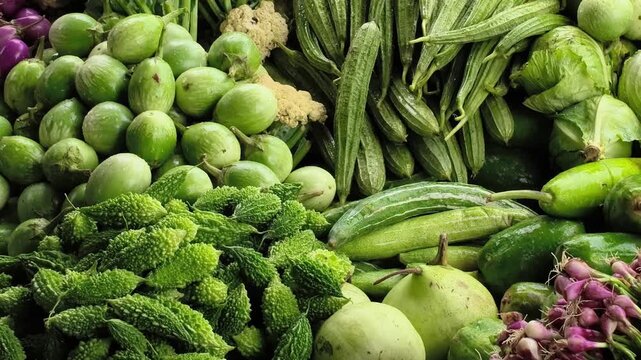 Colorful stack of fresh vegetables in a busy vegetable market. Eggplant, cauliflower, ridge gourd, pointed gourd, bitter melon, tomatoes, spinach, okra, beans, carrots, pumpkins