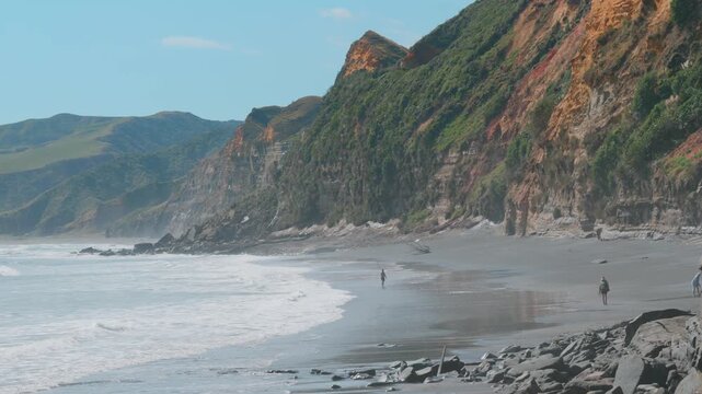 A lone fisherman casts his line into the surf on a rugged beach in  Tunnel Beach, Waikato, New Zealand, with dramatic cliffs rising behind him. ,