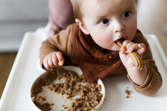 Cute baby infant eating complementary food close up in high chair. Family domestic life. Mom and son having dinner together. blw