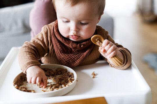 Cute baby infant eating complementary food close up in high chair. Family domestic life. Mom and son having dinner together. blw