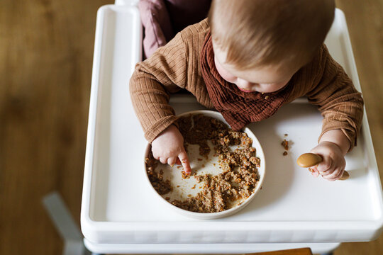 Cute baby infant eating complementary food close up in high chair. Family domestic life. Mom and son having dinner together. blw