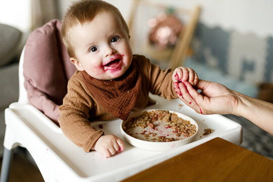 Mother feeding cute happy baby infant with fuit close up, eating complementary food. Family domestic life. Mom and son together, joyful moment