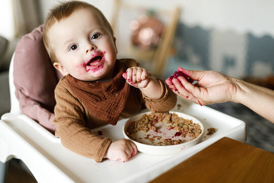 Mother feeding cute happy baby infant with fuit close up, eating complementary food. Family domestic life. Mom and son together, joyful moment