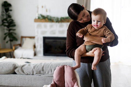 Mother holding cute baby infant with messy face after feeding complementary food. Family domestic life. Mom and son together, joyful moment. Happy Mother's day!