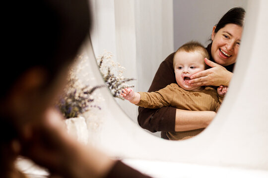 Mother cleaning cute baby infant in modern bathroom after eating complementary food. Family domestic life. Mom washing son face with water in sink, joyful moment. Happy Mother's day!