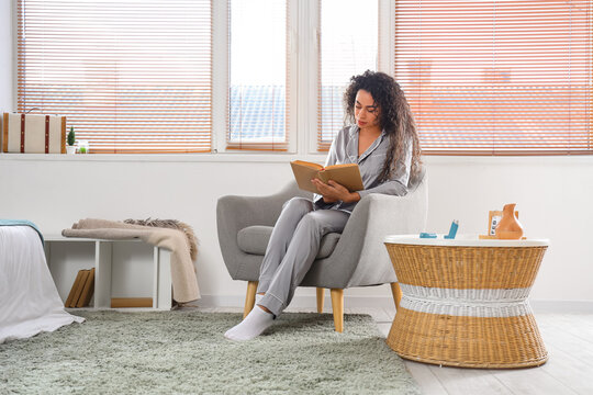Young African-American woman reading book with asthma inhaler on table at home