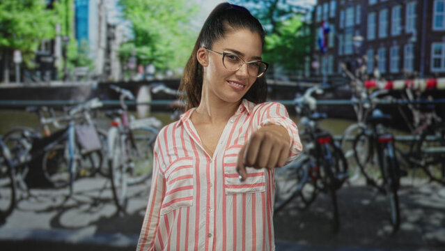 Young hispanic woman fist to chest brotherhood gesture on street in amsterdam canal area with parked bicycles and water; solidarity support.