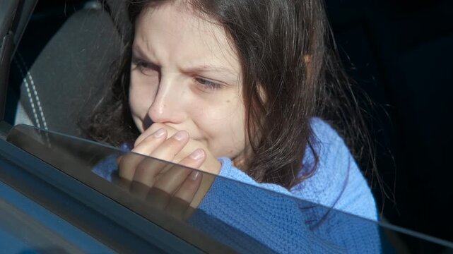 Young girl feeling nauseous and sick in a moving car. Young caucasian girl with long dark hair feeling sick and covering her mouth with her hands, experiencing motion sickness while traveling