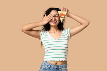Beautiful young happy African-American woman with slice of delicious pizza on beige background