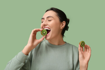 Fototapeta premium Beautiful young woman with tasty kiwi on green background