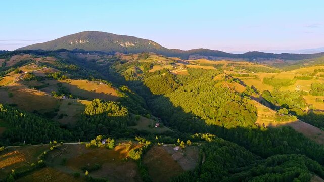 Aerial view of rolling green hills and scattered houses nestled in the Transylvania landscape during golden hour Holbav, Brasov, Romania.