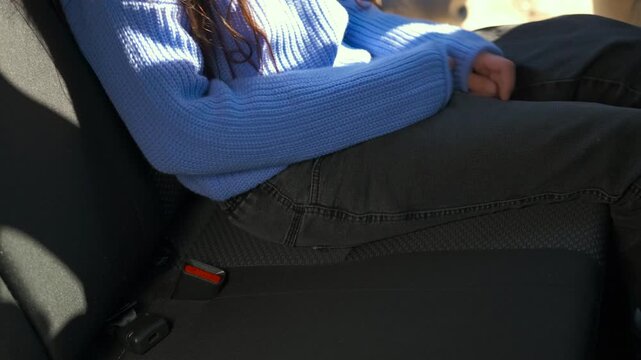 Mother fastens a seat belt on her child in the back seat of a car. Caring mother fastens a seat belt on a teenager in the back seat