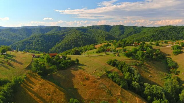 Aerial view of the rolling hills and rural houses of Transylvania with forested mountains under a blue sky in Holbav, Brasov, Romania.