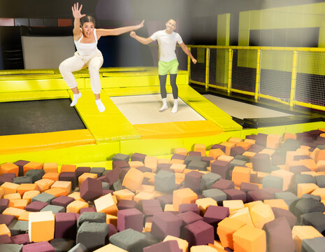 Emotional joyful young girl jumping into foam pit at indoor trampoline arena, with friends leaping nearby
