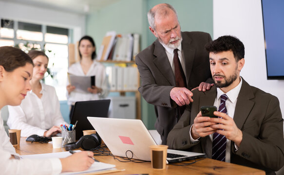 Senior male boss chastises male subordinate for idleness and scrolling of phone, social networks and stealing personal and working time. Procrastination at work, evading official duties.