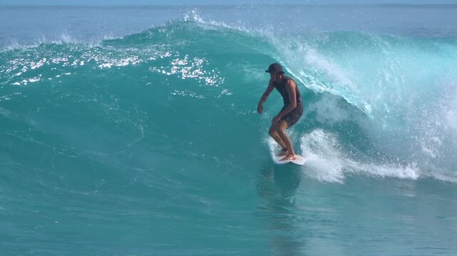 SLOW MOTION: Male surfer glides along clean turquoise wave as it breaks perfectly at Nipussi surf spot. Offshore spray, smooth water and firing wave conditions of a classic Indonesian reef break.