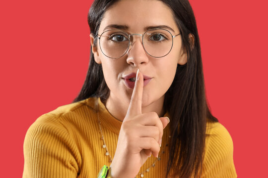 Young gossip woman showing silence gesture on red background, closeup